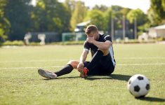 sport, football training, sports injury and people - injured soccer player with ball on field